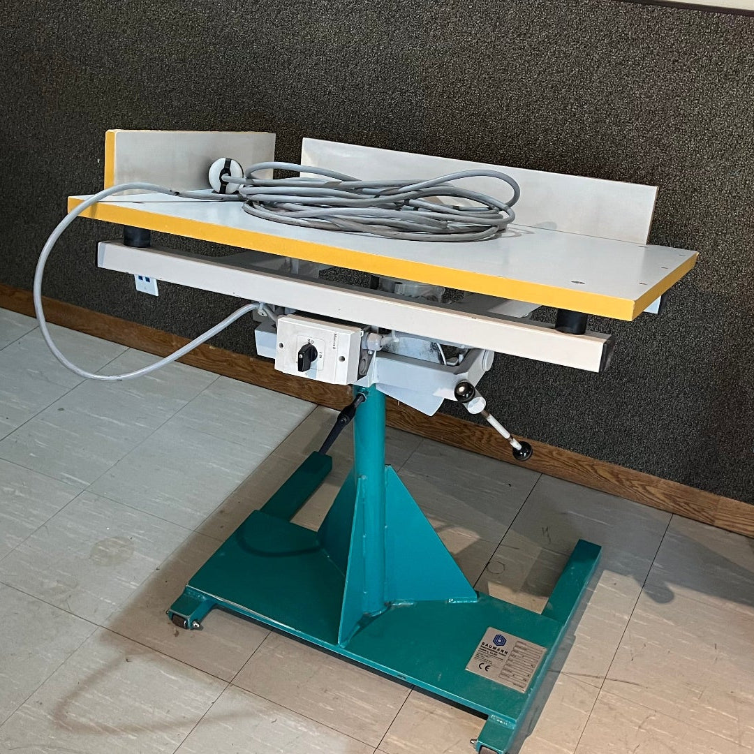 Mechanical lift table with cables on a tiled floor against a dark wall.