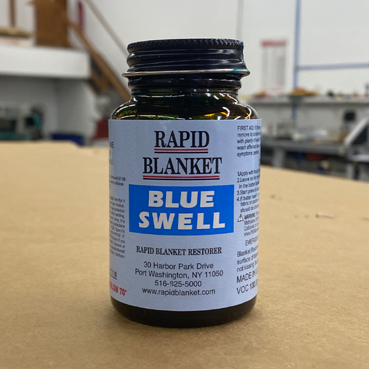 Rapid Blanket Blue Swell bottle of blanket restorer for offset printing press maintenance, shown on workbench background