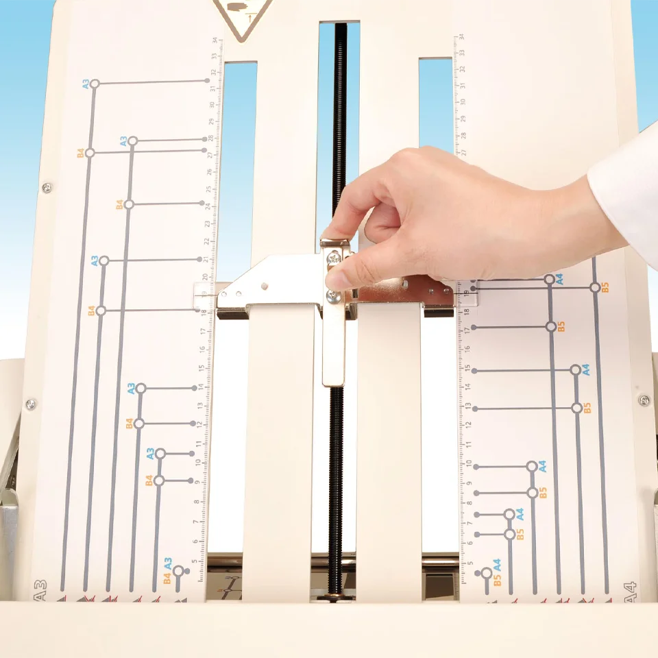Hand adjusting paper guide on MBM 208J paper folder for precise sheet size settings